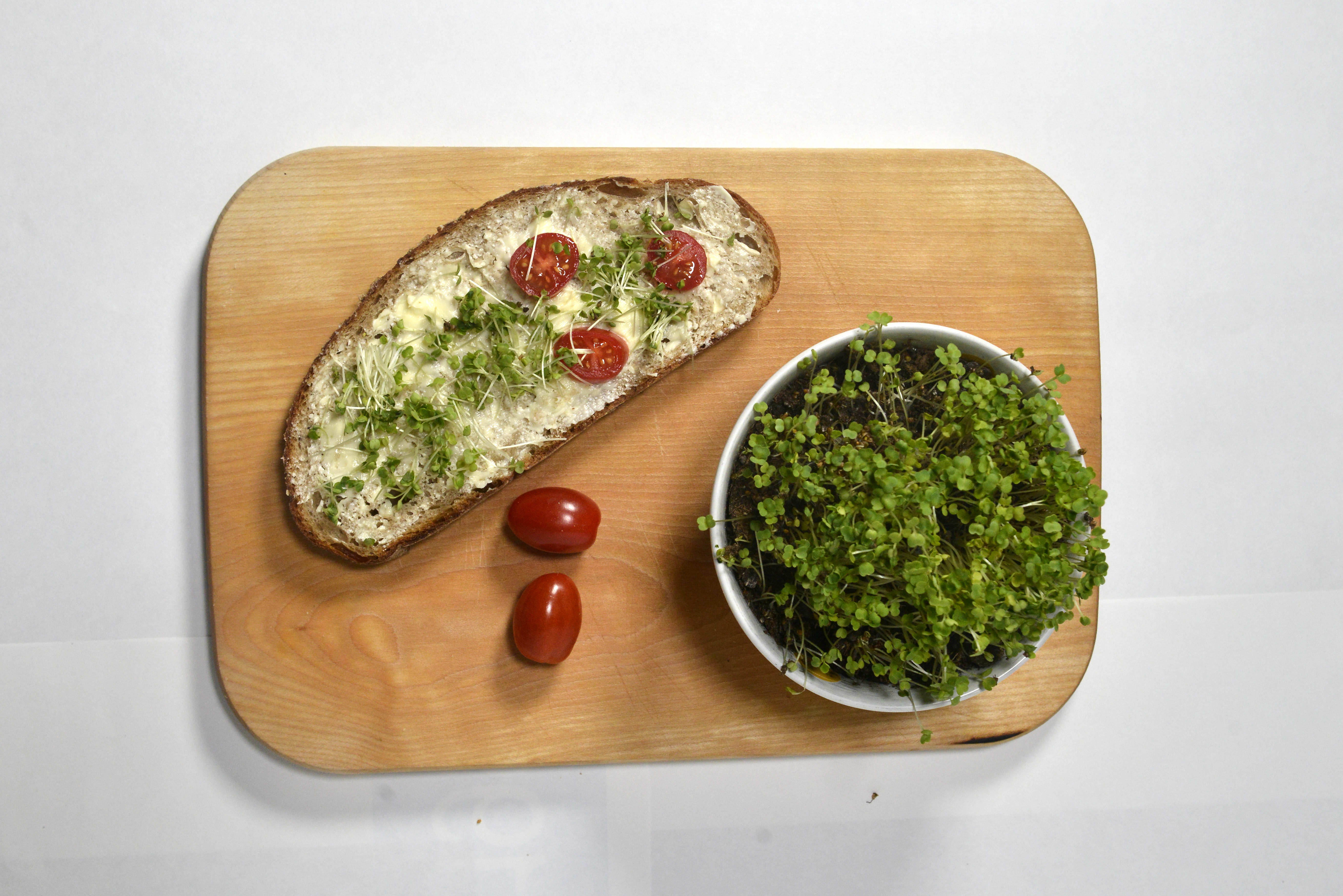 Brot mit Sprossen und Kirschtomaten auf einem Holzbrett