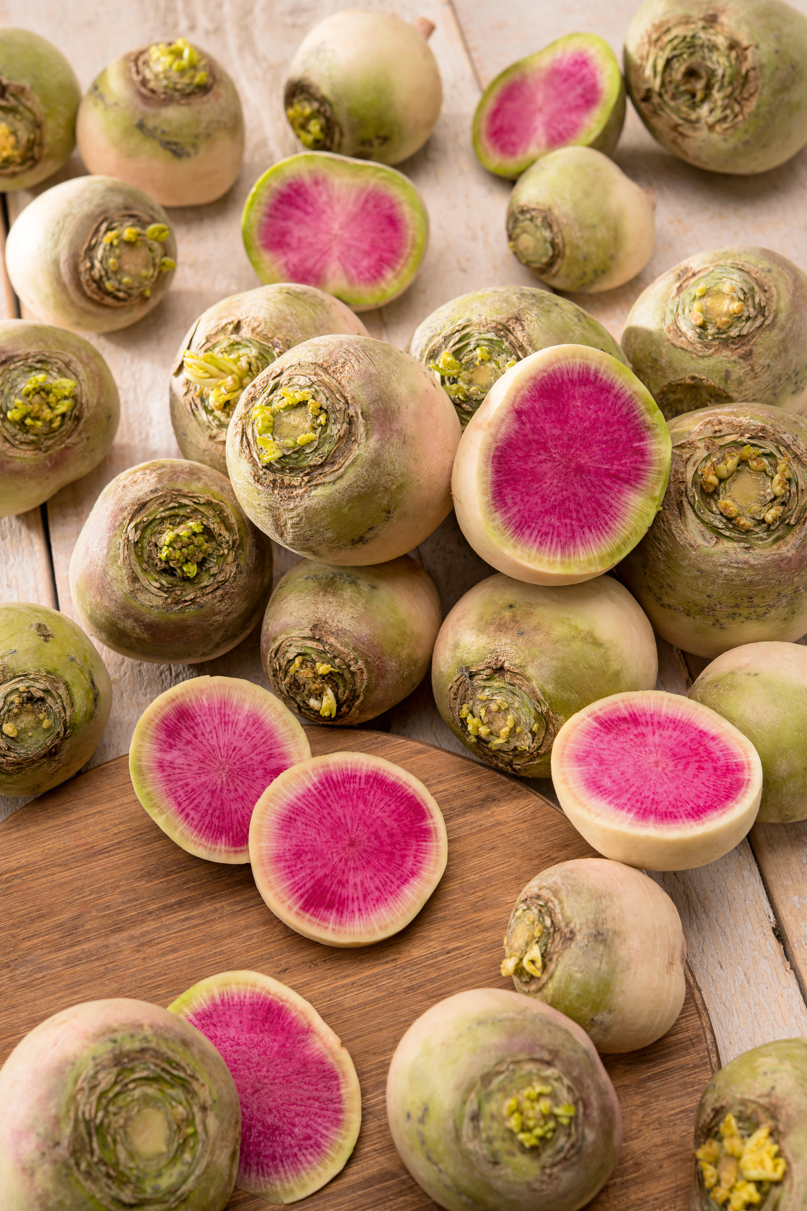 Mehrere Rettich Red Meat von Samen-Fetzer mit weißgrüner Schale und aufgeschnittenem, leuchtend pink-rosa Inneren – außergewöhnlicher Rettich mit süßlich-nussigem Geschmack.