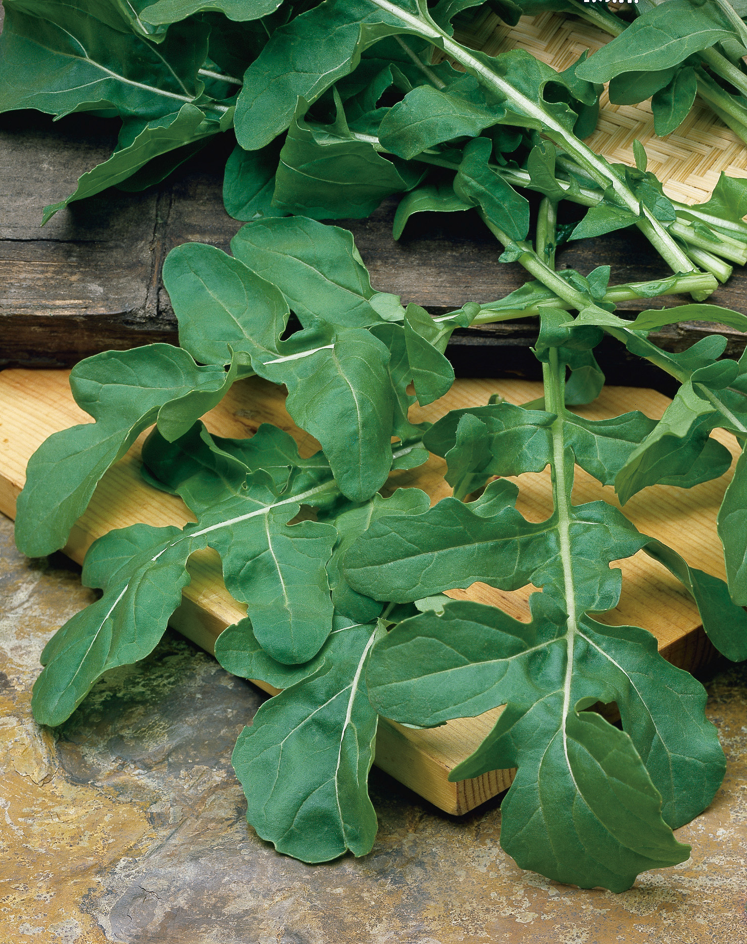 Nahaufnahme von frischem Rucola (Rauke) mit dunkelgrünen, länglichen, leicht gezackten Blättern auf Holzbrett