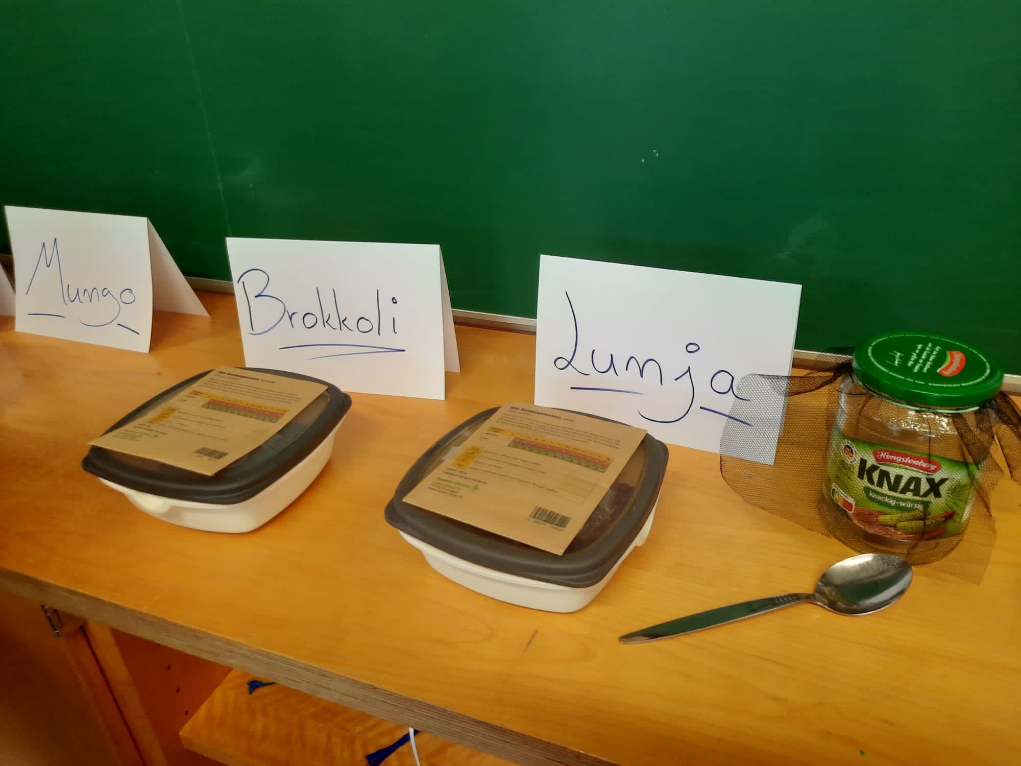 Tisch mit Mungobohnen, Brokkoli und Lumja in Schalen, daneben ein Glas Knax und ein Löffel