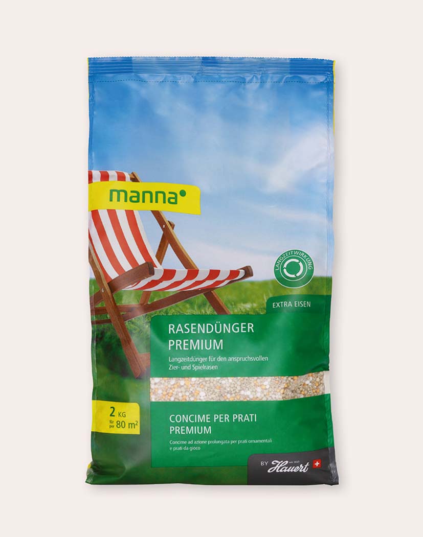Packung 'manna Rasendünger Premium' 2 kg vor grüner Wiese mit Liegestuhl-Motiv; Langzeitdünger für Zier- und Spielrasen, Extra-Eisen, reicht für ca. 80 m²