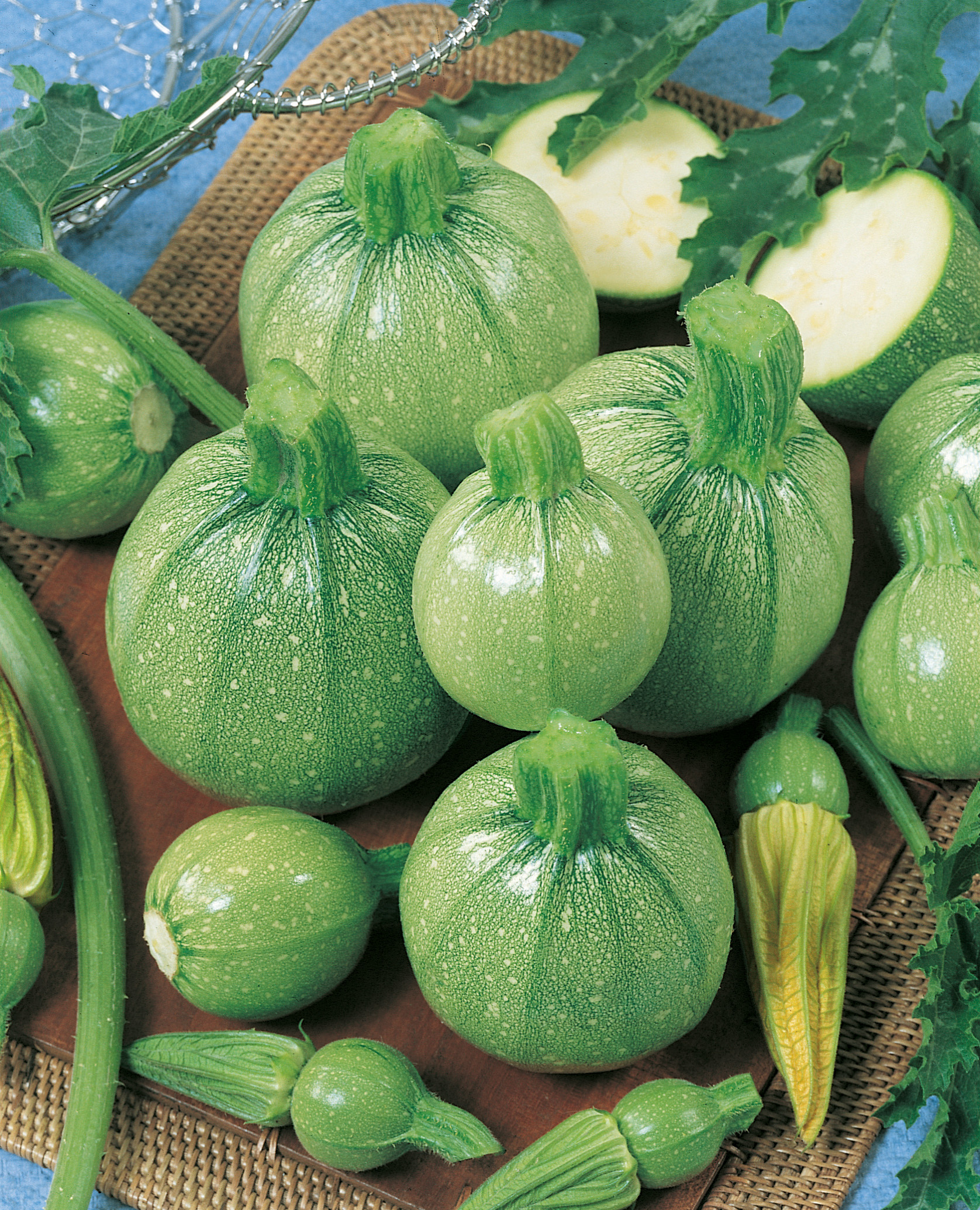 Mehrere runde grüne Zucchini (Kugelzucchini) unterschiedlicher Größe auf Holzbrett, einige halbiert, mit Stielansätzen und Zucchiniblüten, Nahaufnahme