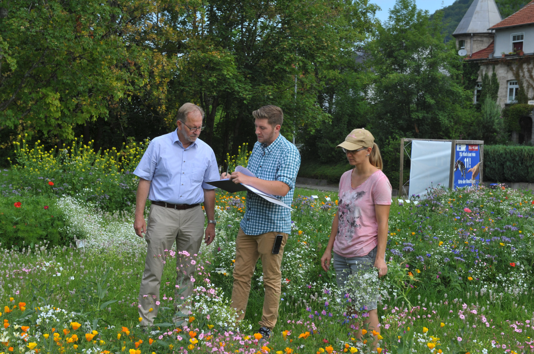 Drei Personen besprechen eine Blumenwiese in blühender Landschaft