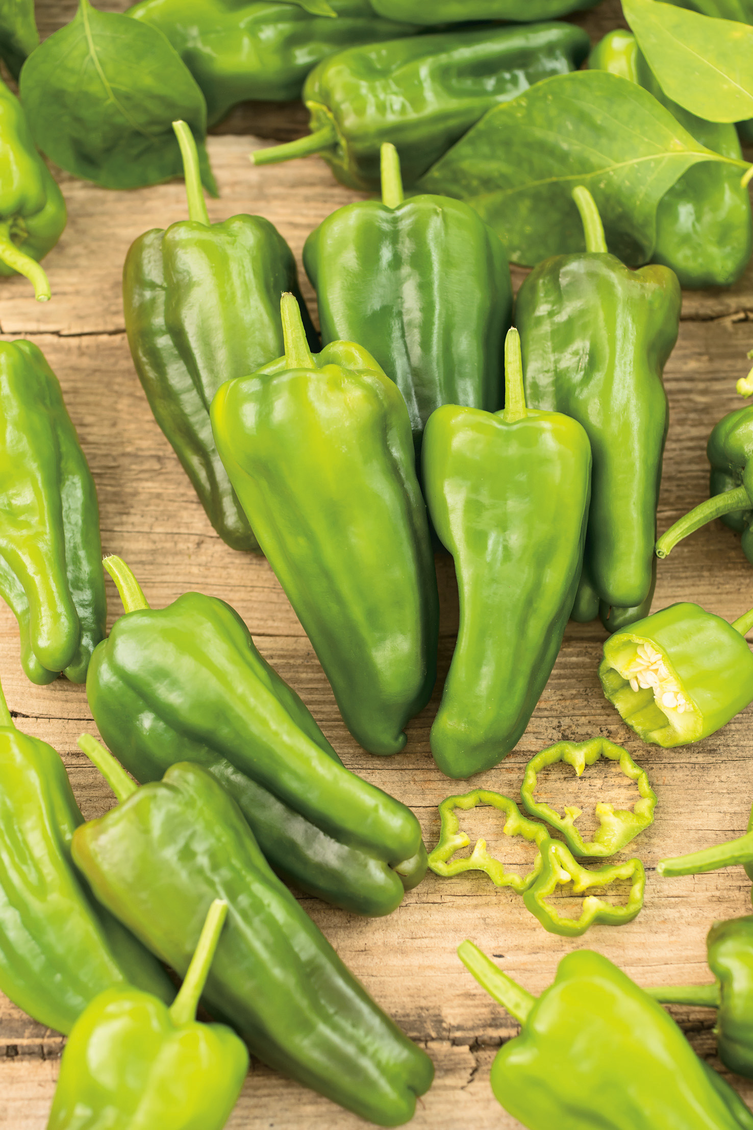 Frische grüne Paprika auf rustikalem Holzbrett, mehrere ganze und geschnittene Früchte mit Stielen und Ringen