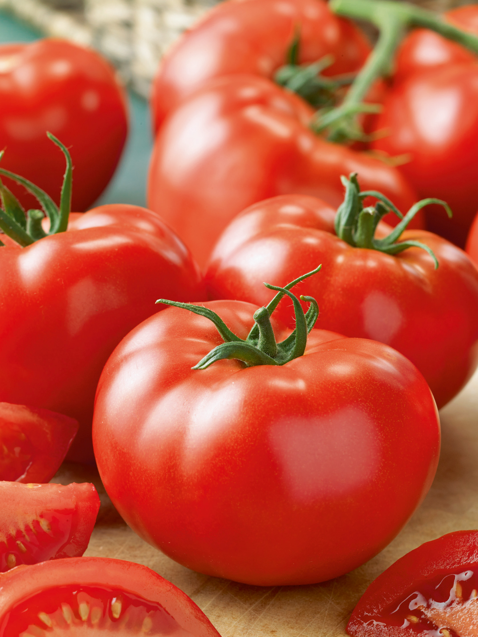 Nahaufnahme glänzender roter Tomaten mit grünen Stielen und aufgeschnittenen Tomatenstücken auf einem Schneidebrett