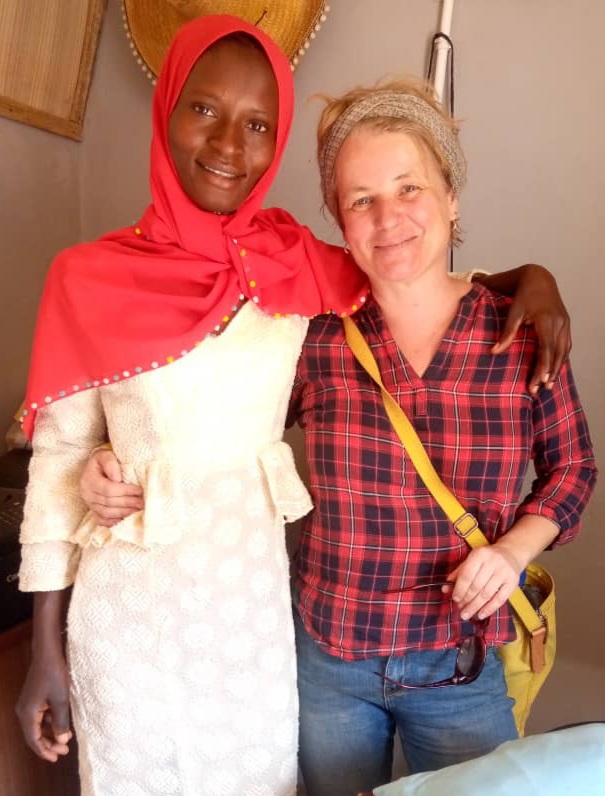 Freundliches Portrait zweier Frauen, eine in rotem Kopftuch und eine in karierter Bluse, die sich umarmen.