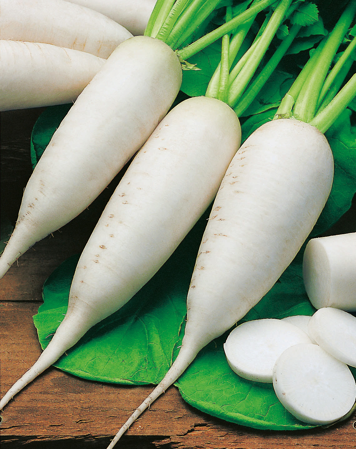 Frischer weißer Daikon-Rettich mit Blattgrün, drei ganze Wurzeln und einige aufgeschnittene Scheiben auf Holzuntergrund