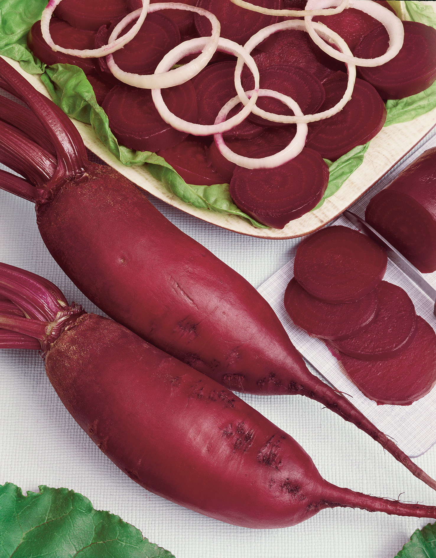 92830_Rote Bete Forono Zwei rote Bete-Knollen und geschnittene Scheiben auf einer Servierplatte mit Salatblättern und Zwiebelringen