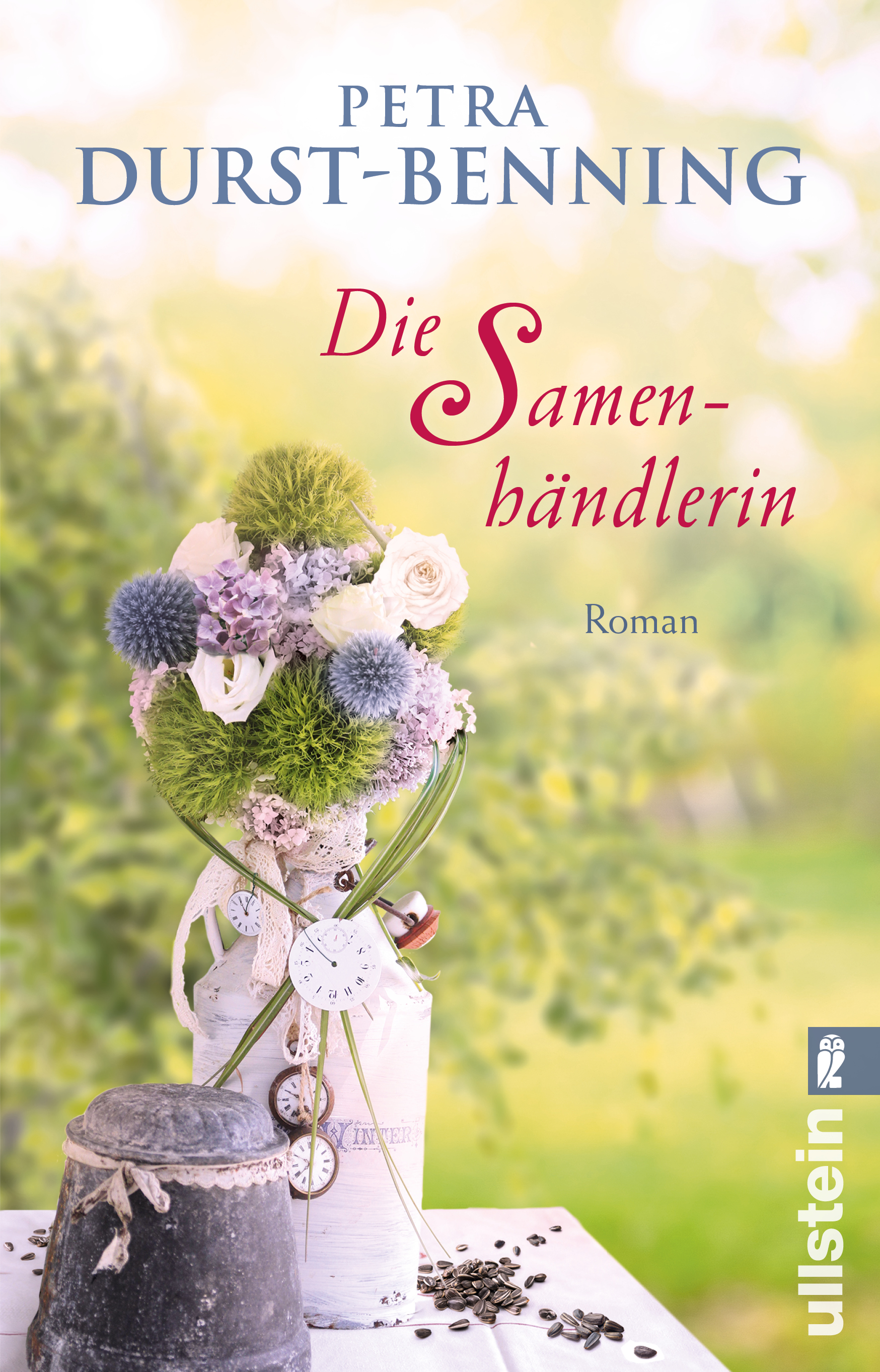 Buchcover von 'Die Samenhändlerin' von Petra Durst-Benning: rustikales Blumenarrangement in Weiß und Grün in Vase, Uhranhänger, verstreute Samen auf Tisch, sonniger, verschwommener Gartenhintergrund, Ullstein-Logo.