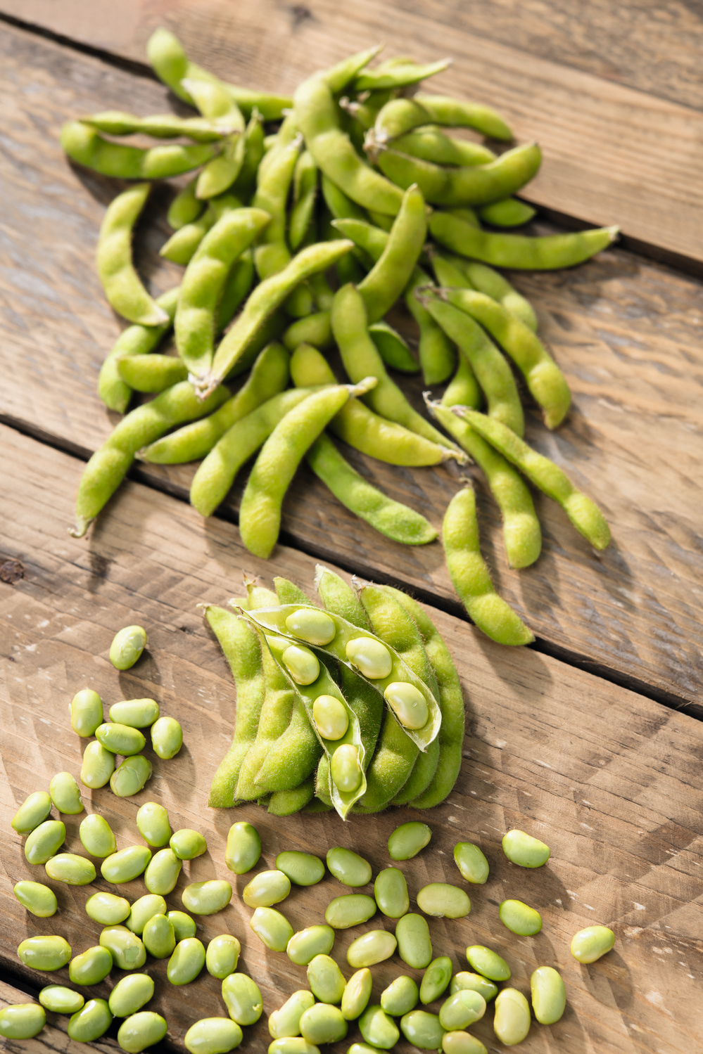 Nahaufnahme von frischen, grünen Edamame-Schoten und herausgelösten Sojabohnen auf rustikalem Holztisch