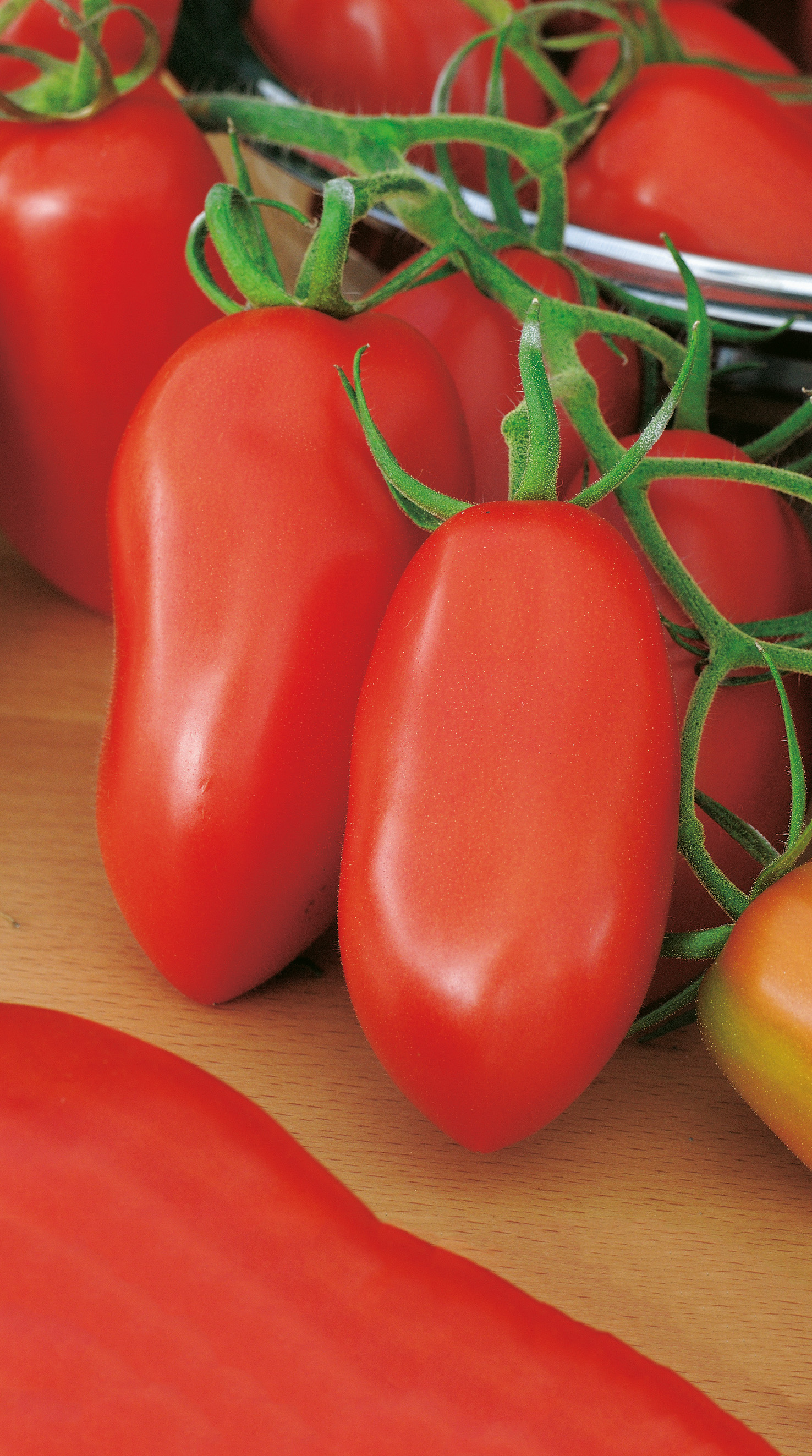 Nahaufnahme von roten, länglichen Roma-Tomaten an grüner Rispe auf Holzuntergrund