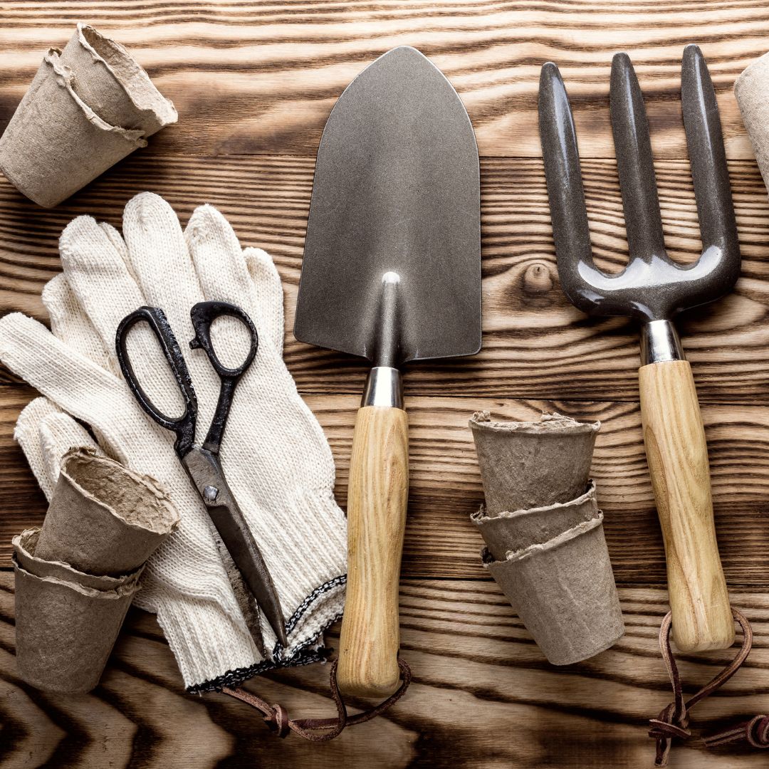 Hochwertige Gartenwerkzeuge und Zubehör Gartenwerkzeuge wie Schaufel, Grabegabel, Handschuhe und Papiertöpfe auf einem Holztisch