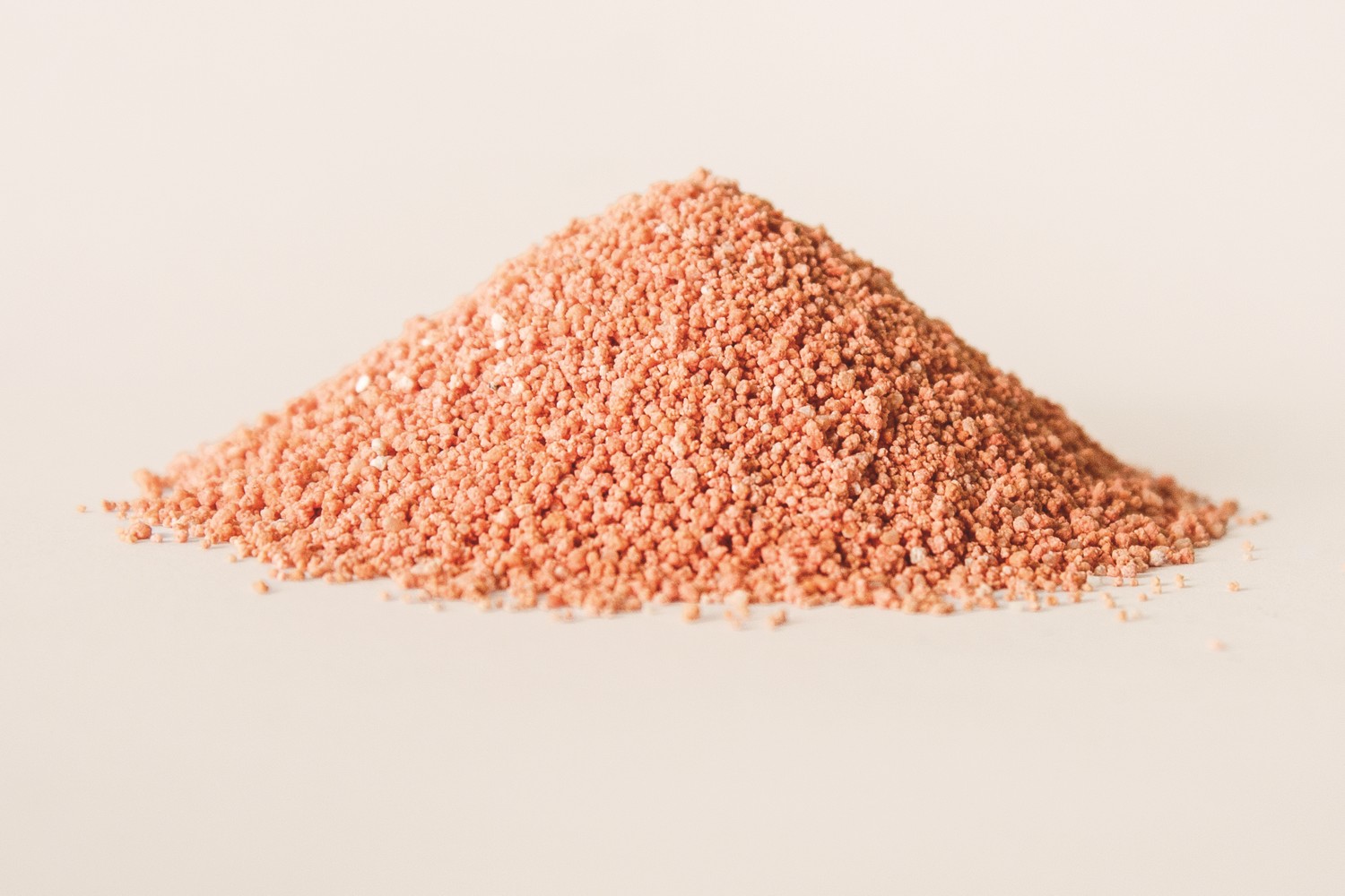 Nahaufnahme eines Haufens rosa-orangefarbenen Granulats mit feiner Körnung auf hellem Hintergrund